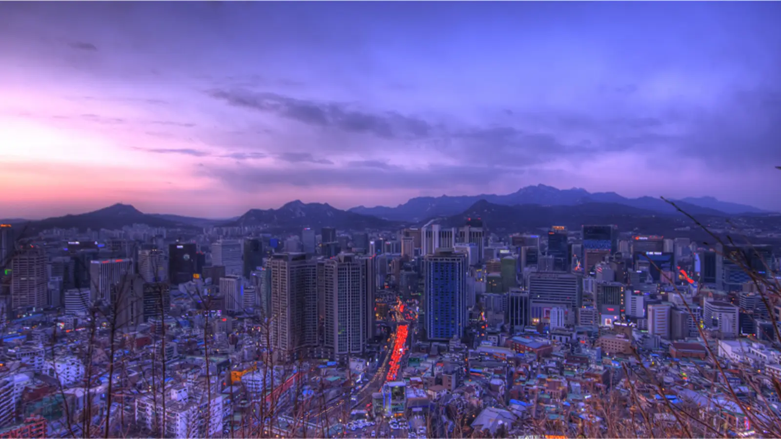 Seoul skyline at dusk with city lights and mountains behind the city